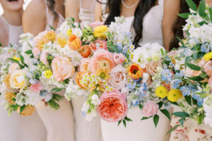 Wedding party holding vibrant bouquets of pastel flowers in soft dresses; focus on floral arrangements and greenery.