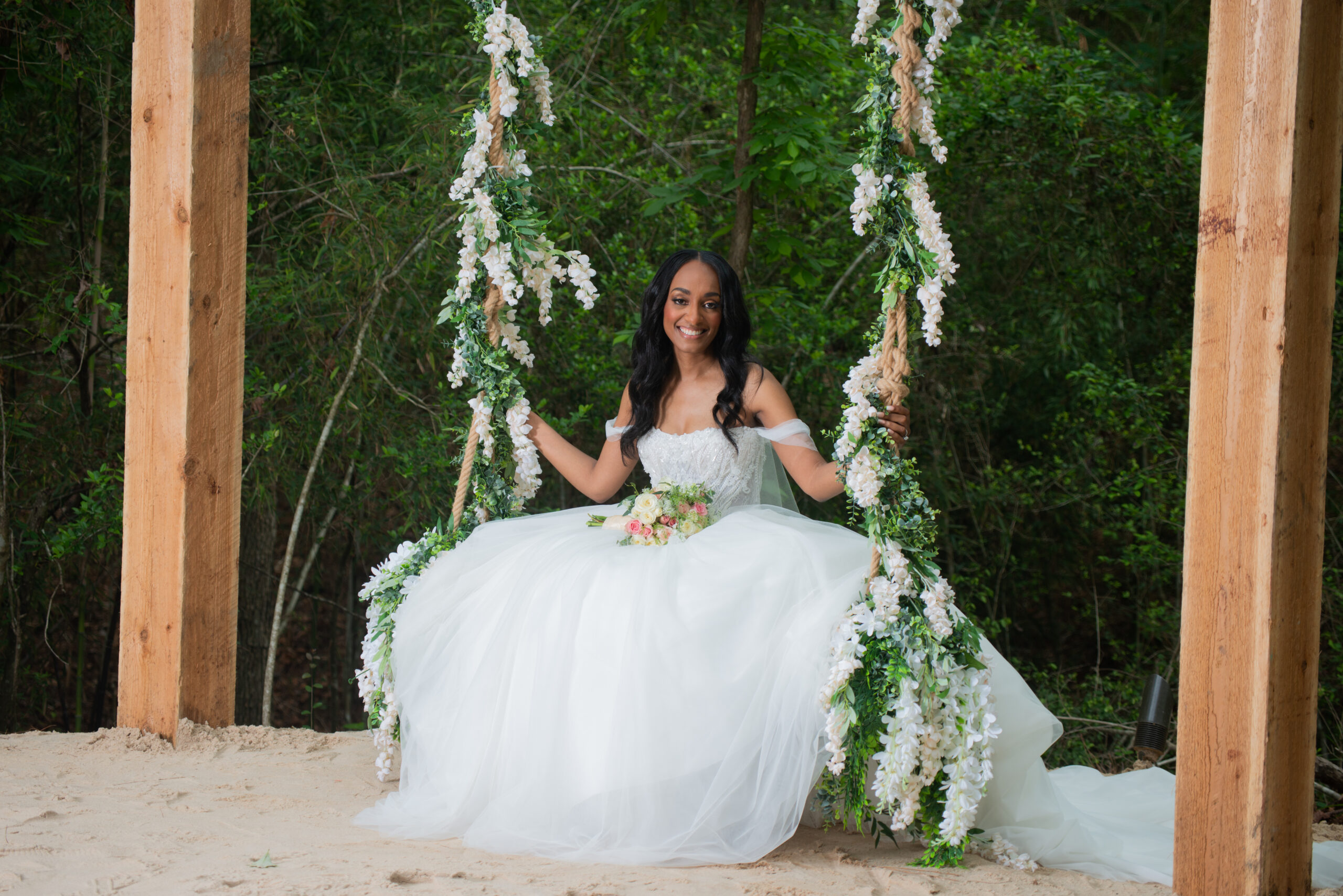 Bride in a white wedding gown with a swing covered in hanging white blossoms.
